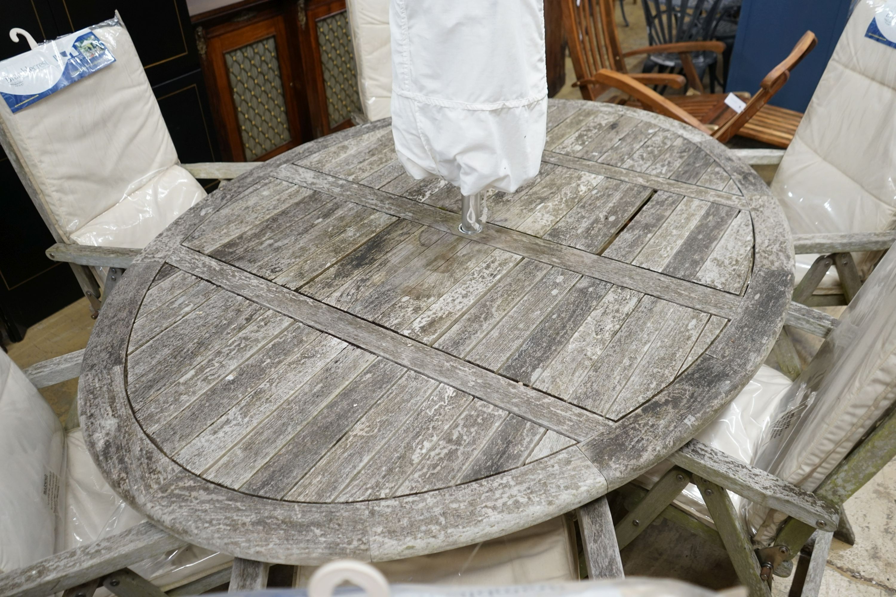 A Bramblecrest weathered teak oval garden table, width 200cm, depth 150cm, height 74cm eight folding teak reclining elbow chairs, seat pads and parasol with stone base